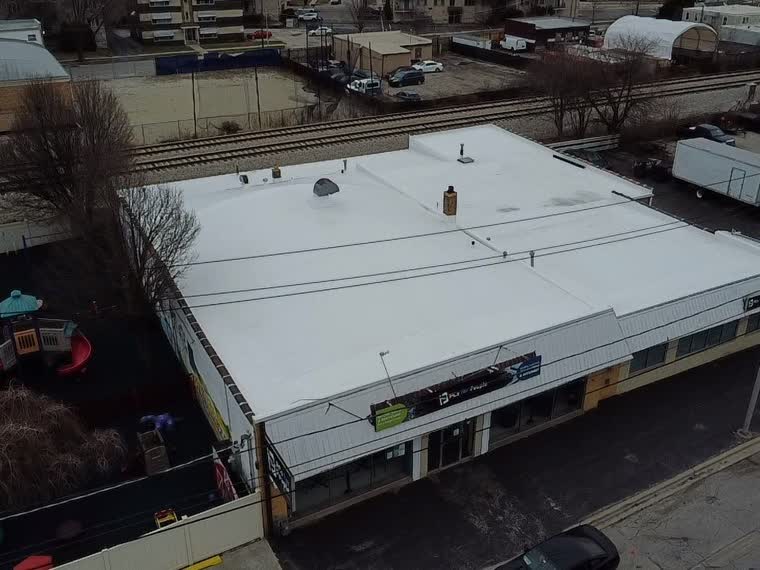 Completed white roof over a commercial building on an urban block.