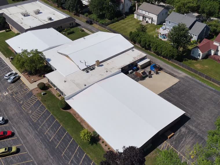 Reflective roof over a low commercial building among mature deciduous canopy.