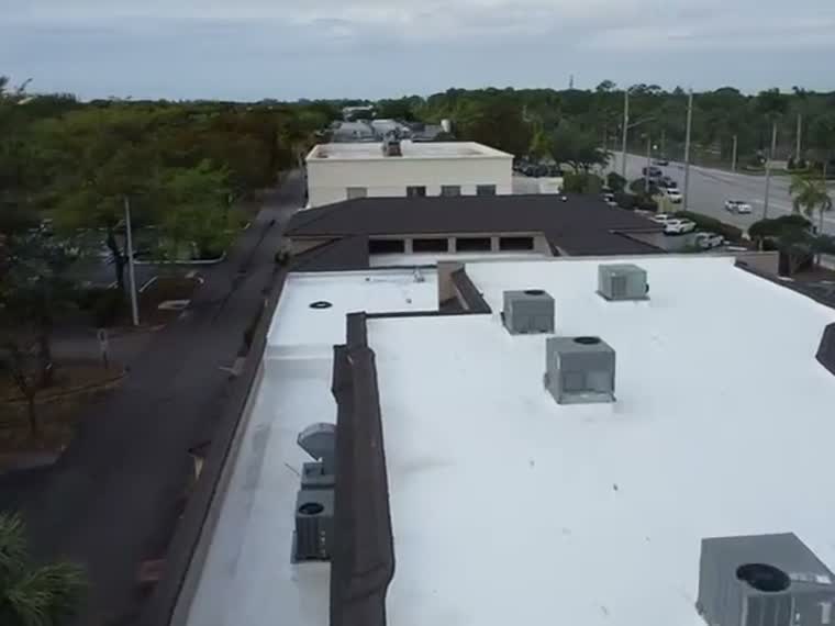 Flyover of a commercial roof and the parking area behind it.