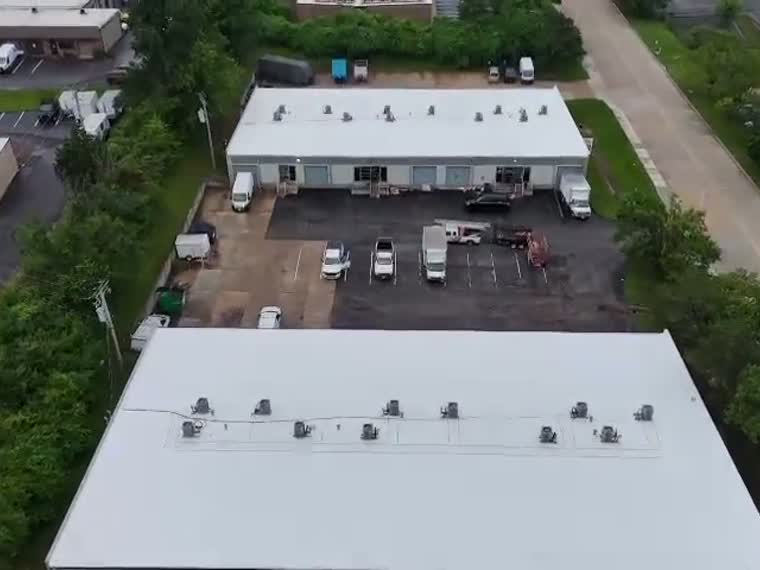 Completed white roof surrounded by mature deciduous canopy.
