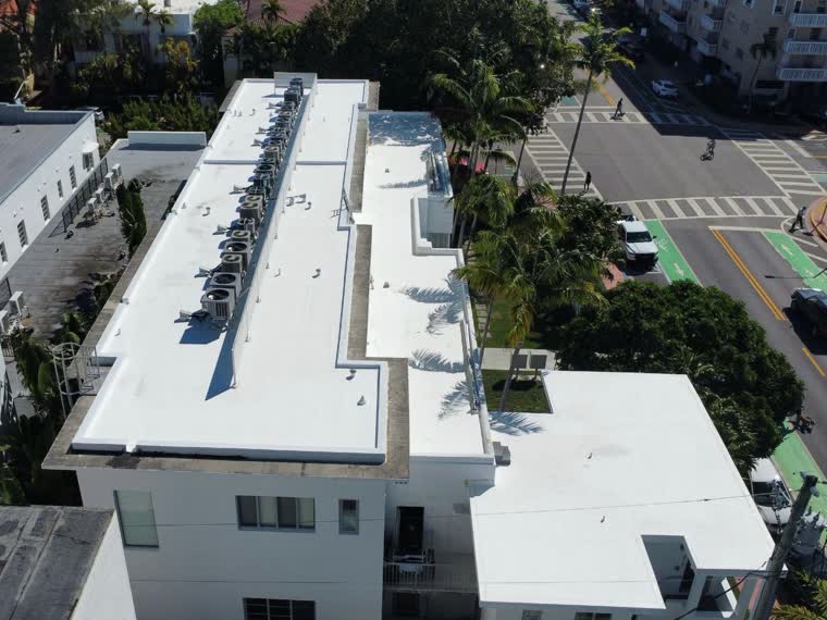 Completed white membrane on a low-rise building, palms at the perimeter.