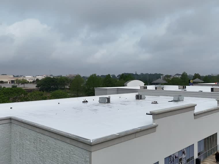 Completed white roof under overcast sky, mechanical screening at the ridge.