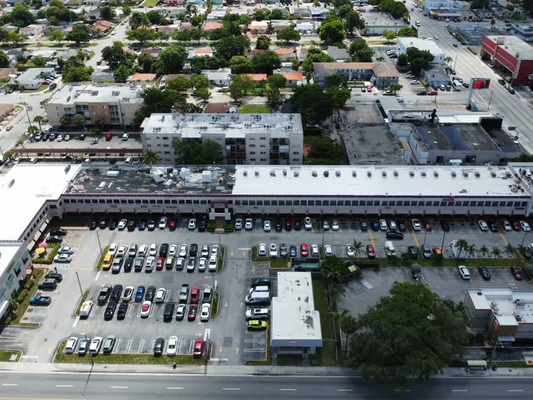 Shopping centre roofs from above, parking field and access lanes visible.