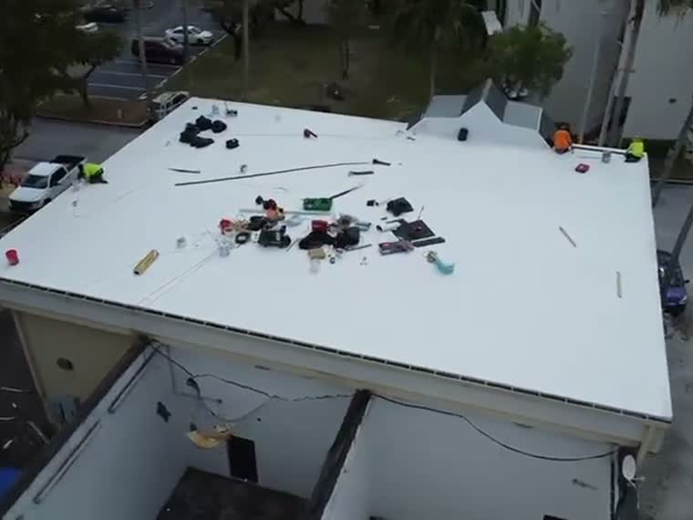 Close pass over a completed white roof with equipment set inside the field.