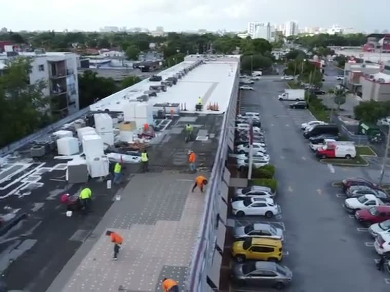 Crew working along a retail strip roof with traffic moving below.