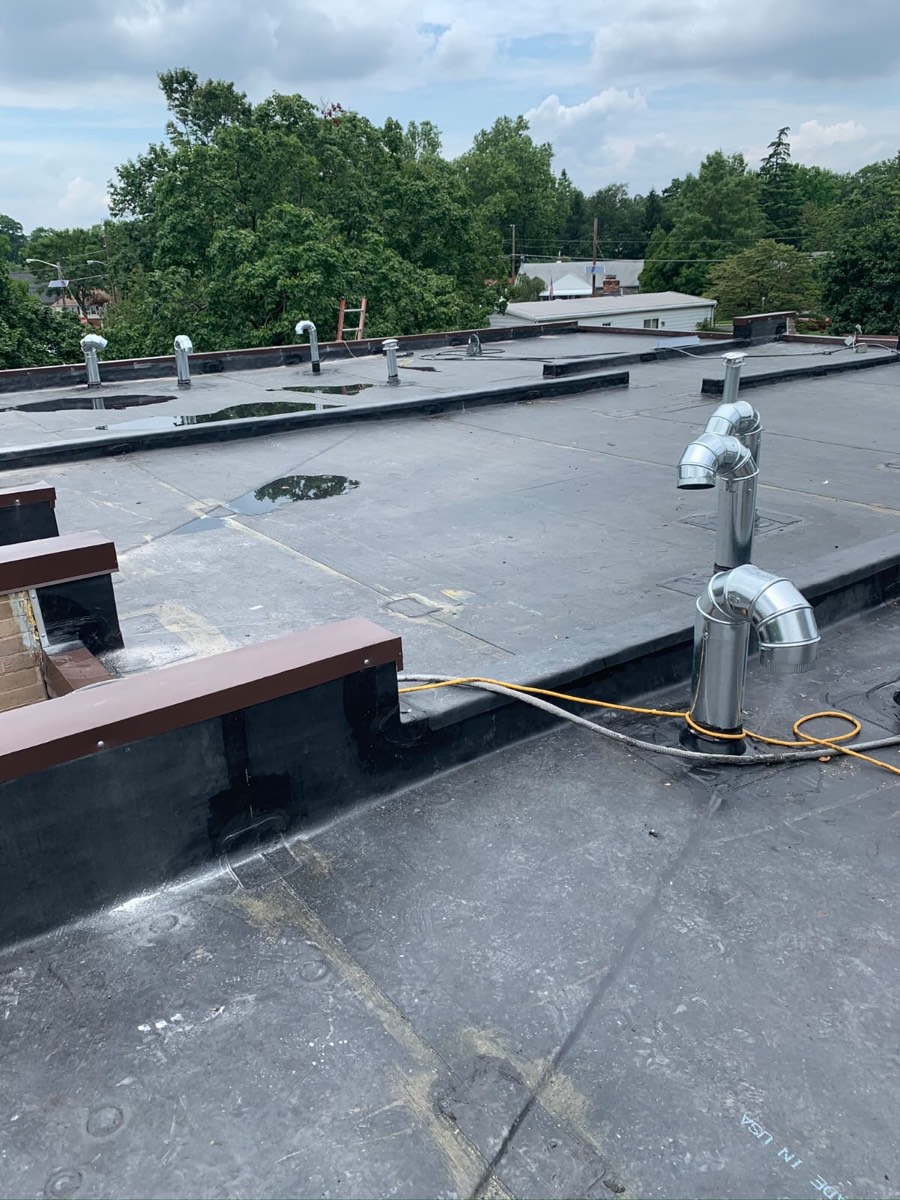 Aging dark low-slope roof with mechanical equipment and conduit before replacement