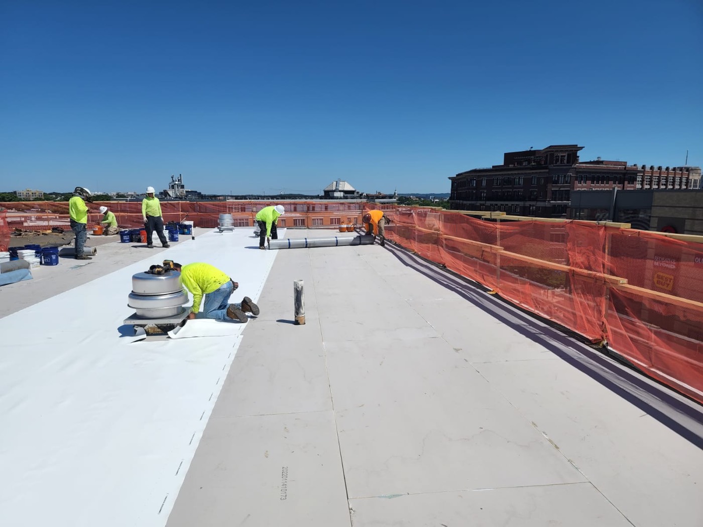 Roofing crew working across a large low-slope commercial roof with the Washington DC skyline behind them