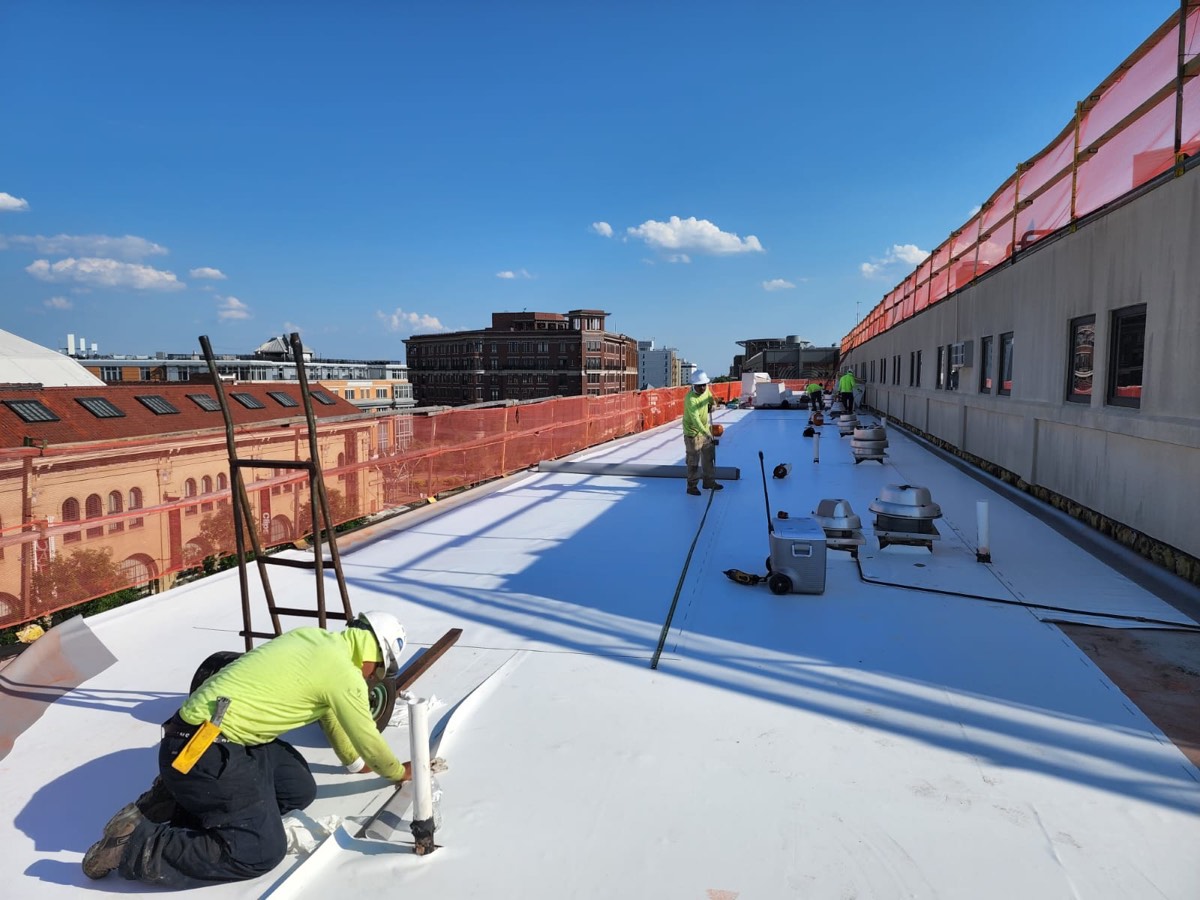 Roofers rolling out and fastening single-ply roofing membrane