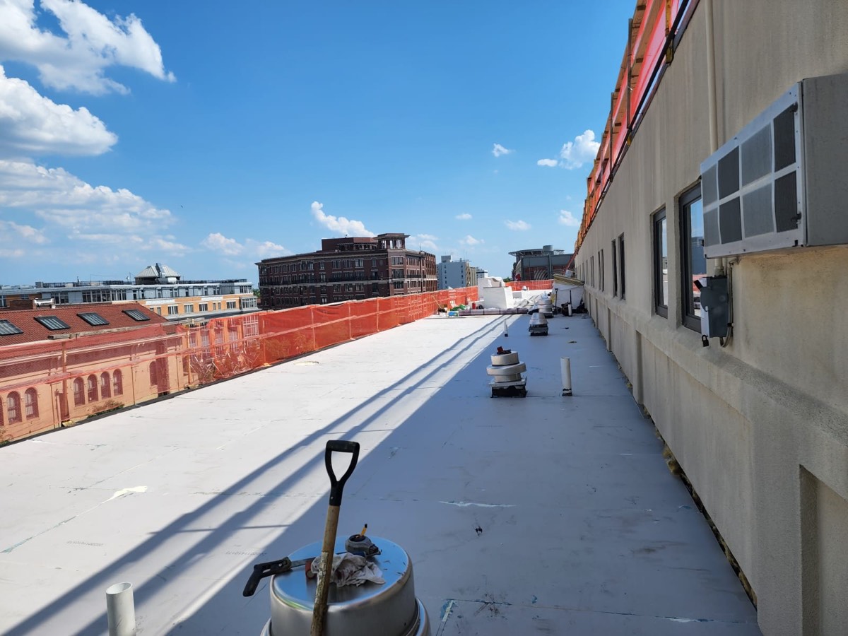 Crew installing single-ply membrane on a long low-slope commercial roof behind a brick parapet
